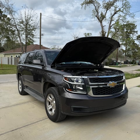 Black Chevrolet Tahoe SUV with open hood parked in driveway, residential street in background