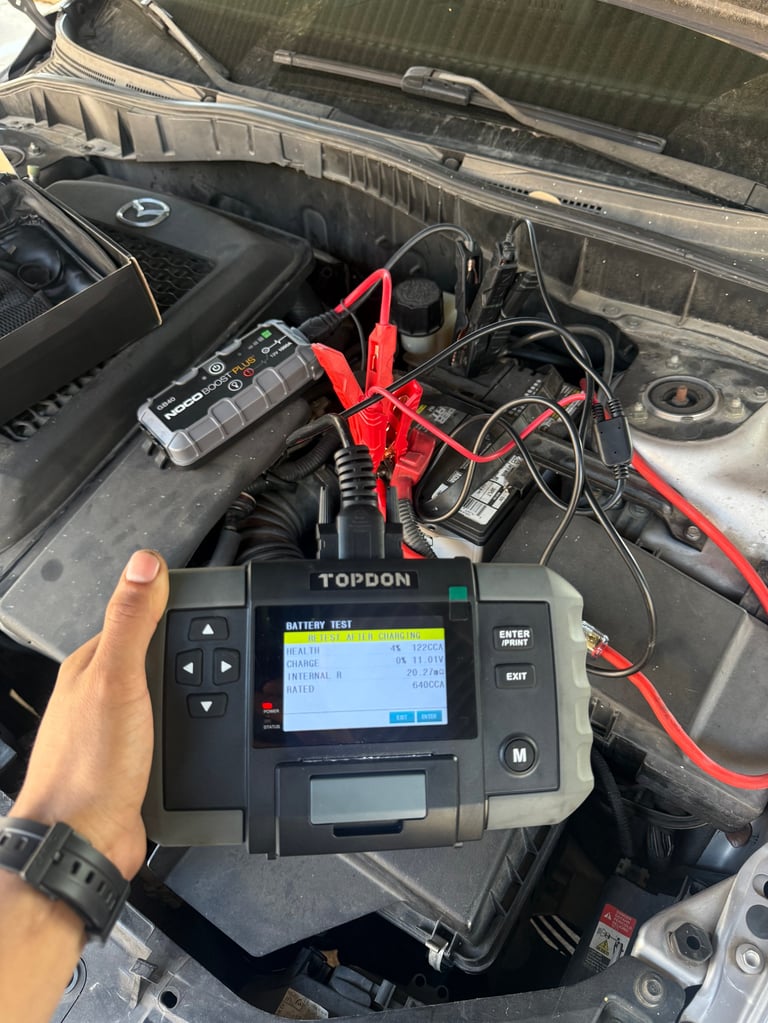 Technician holding TOPDON battery diagnostic tester connected to car engine with red and black jumper cables
