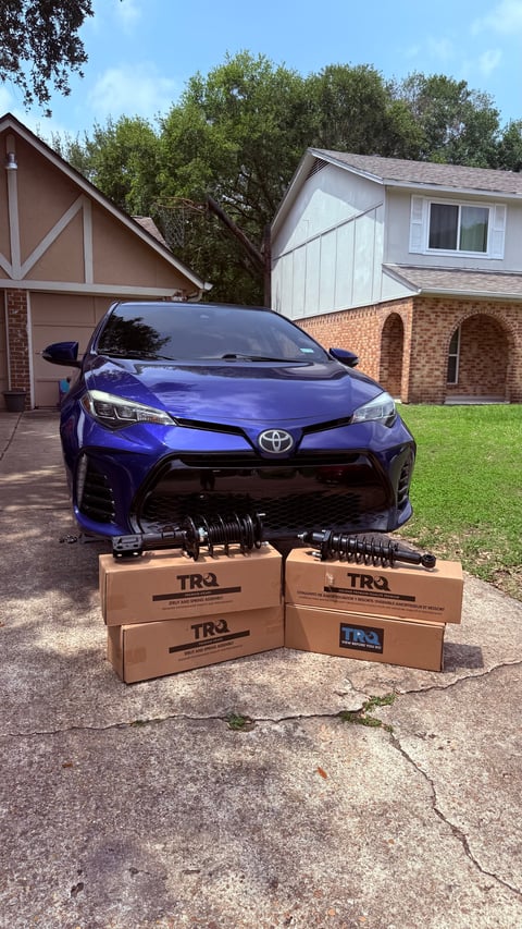 Blue Toyota Corolla with TRQ suspension parts boxes displayed in front on residential driveway
