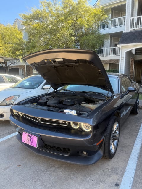 Black Dodge Challenger with open hood displaying engine in residential parking lot