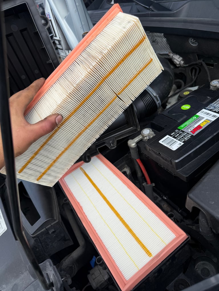 Hand holding a dirty air filter above a clean replacement filter in an open car engine bay