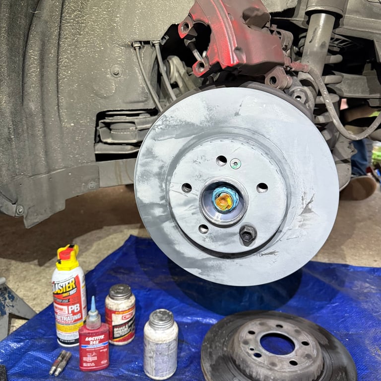 Brake disc and rotor removal during vehicle maintenance, with cleaning supplies and old rotor on blue work mat